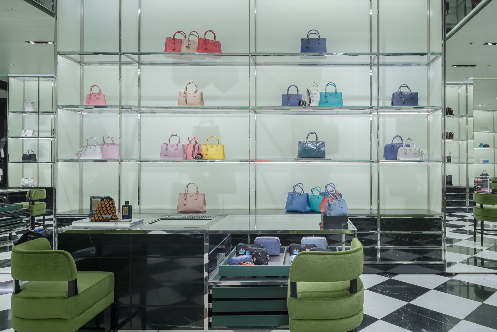 Elegante exhibición de bolsos de lujo en una tienda Prada, con bolsos coloridos dispuestos en estantes de vidrio y sillas verdes en primer plano.