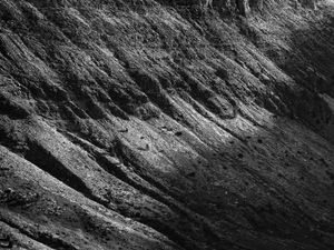 Fotografia en blanc i negre d'un vessant de muntanya rocós i pronunciat, amb prominents crestes diagonals i textures il·luminades per una dramàtica llum natural.