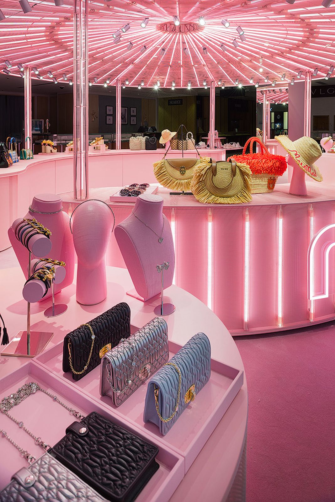 Exhibición de bolsos, joyería y sombreros de Miu Miu en una tienda pop-up rosa brillantemente iluminada.