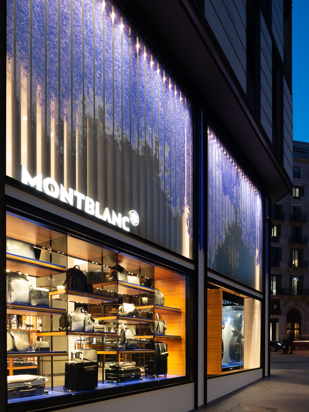 Exterior de tienda Montblanc mostrando estantes de bolsos y equipaje con diseño de ventana azul iluminado.