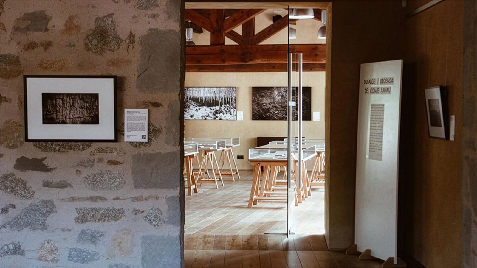 Vista hacia una sala de galería con fotos enmarcadas en las paredes y vitrinas sobre soportes de madera.