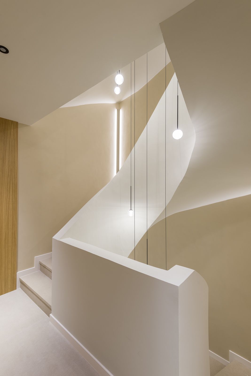 Architectural perspective of a modern spiral staircase featuring smooth beige plaster walls, a sweeping curved balustrade, and slender suspended black wires holding glowing orb pendant lights in the central stairwell void.