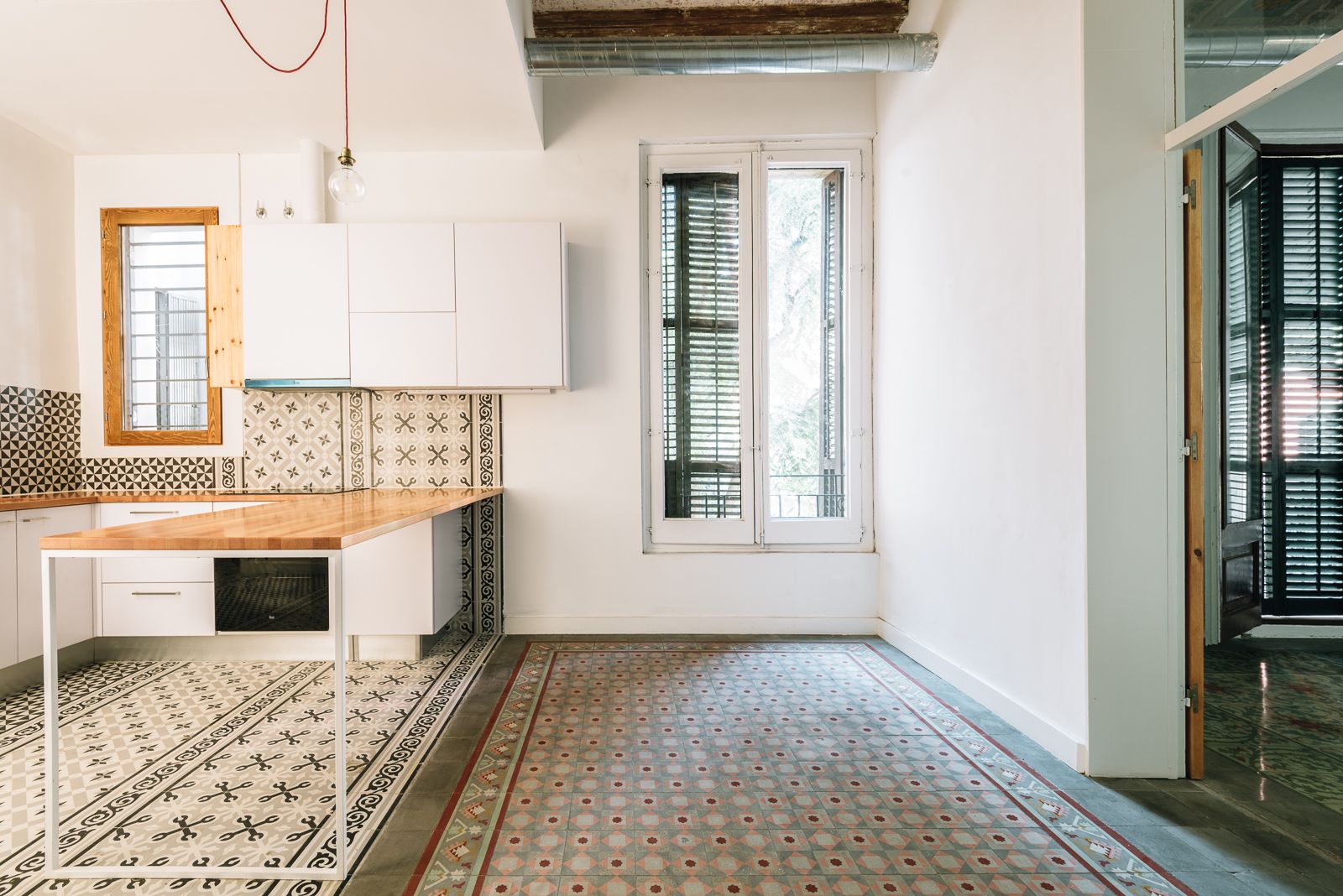 Cocina moderna con baldosas estampadas, acentos de madera y una mesa de trabajo minimalista.