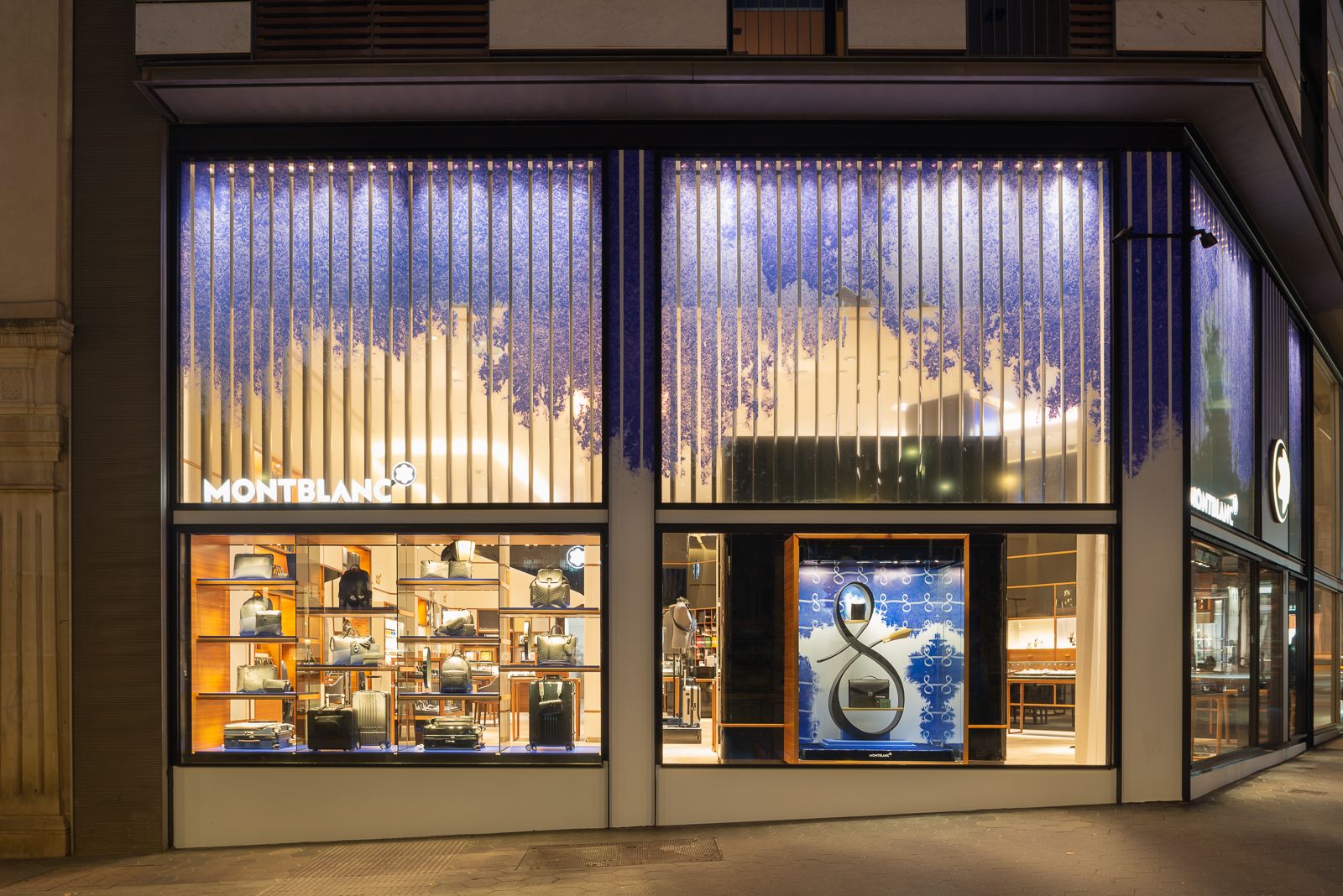 Exterior de tienda Montblanc por la noche con ventanas iluminadas que exhiben bolsos y accesorios, con elementos de diseño modernos y sofisticados.
