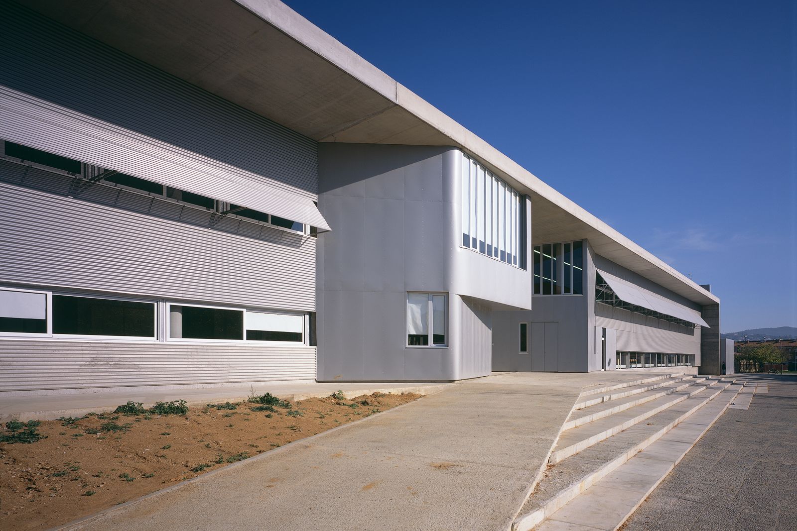 Modern architectural details of Fontajau High School, showcasing its sleek lines and large windows under a clear blue sky.