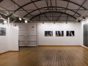 Galería espaciosa con obras de arte en las paredes, suelos de madera y techo metálico expuesto.