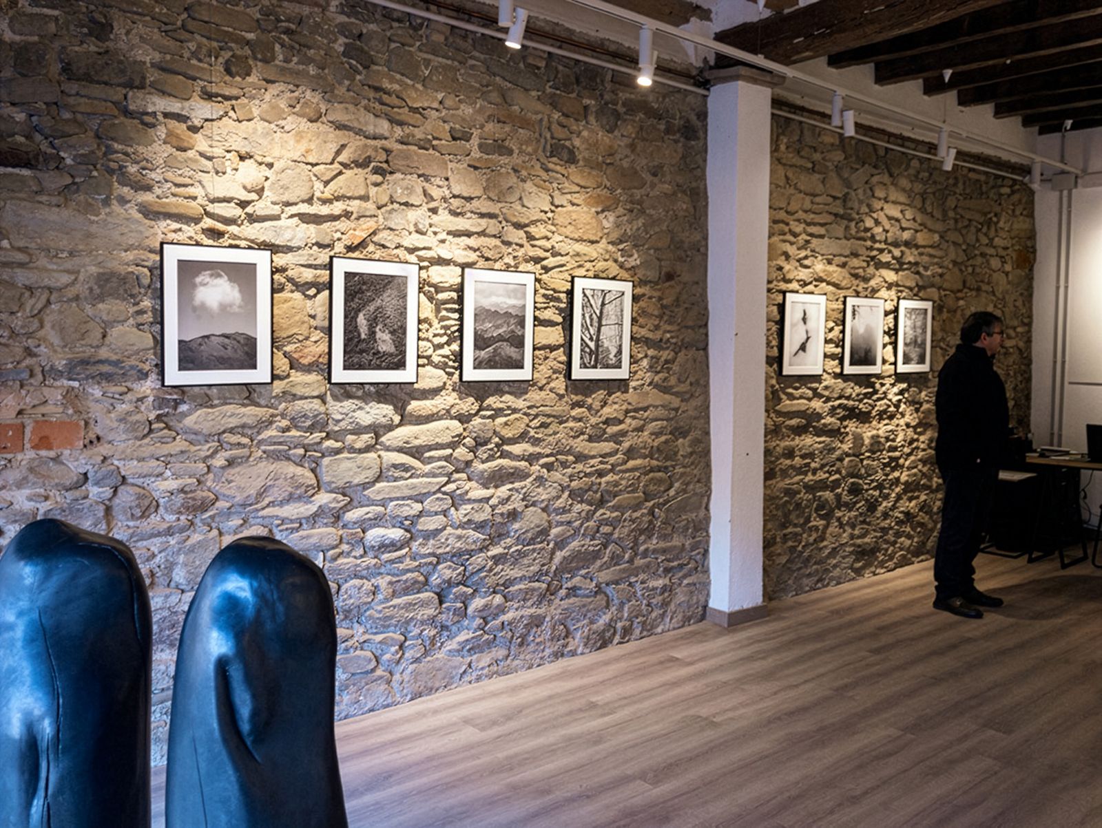 Exposición de fotografía con fotos de paisajes enmarcadas en blanco y negro en una pared de piedra.