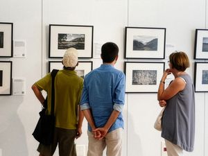 Tres personas examinando de cerca fotografías de paisajes enmarcadas en una pared de galería.