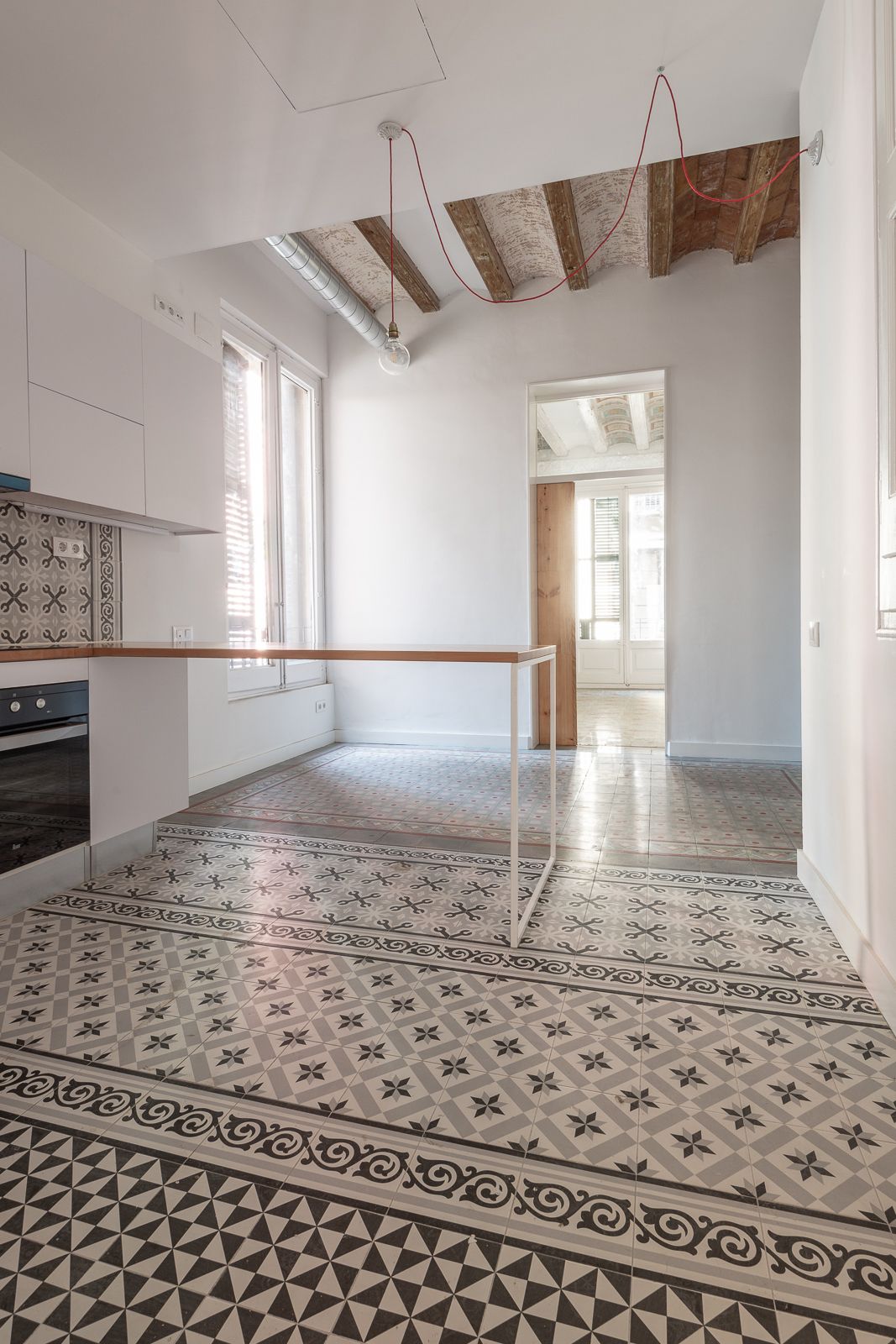Cocina luminosa con baldosas de suelo estampadas, vigas de madera expuestas y una mesa de trabajo minimalista.