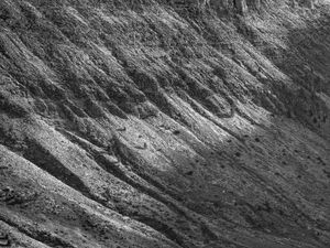 Fotografia en blanc i negre d'un vessant de muntanya rocós i pronunciat, amb prominents crestes diagonals i textures il·luminades per una dramàtica llum natural.