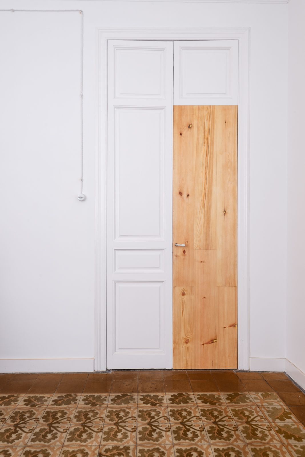 Puerta blanca con un panel parcialmente de madera y baldosas de suelo estampadas.