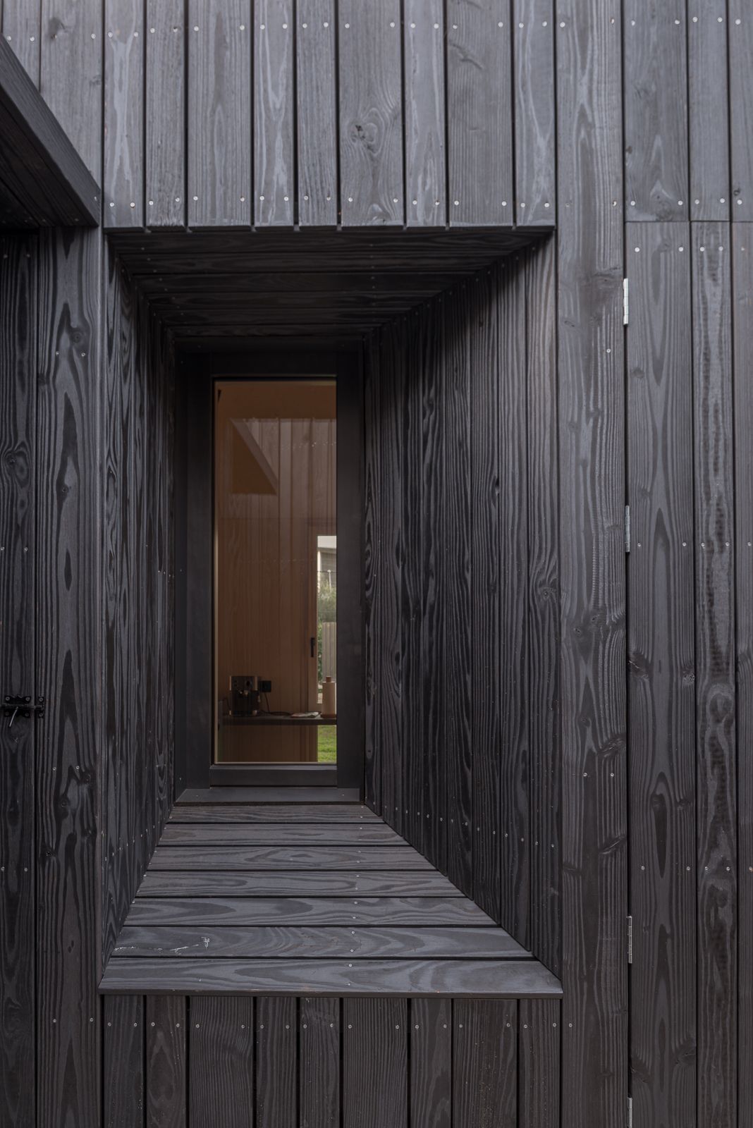 Primer plano de un exterior revestido de madera oscura con una ventana empotrada, mostrando artesanía y diseño detallados.