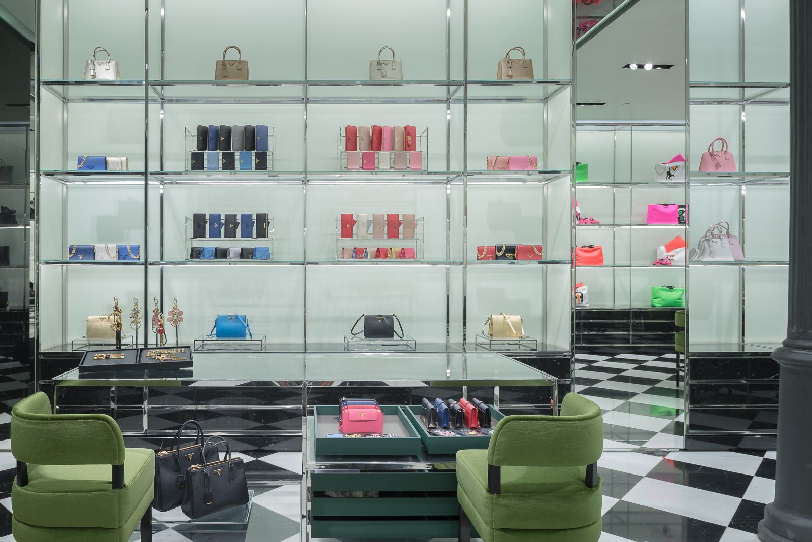 Interior de tienda de lujo con una exhibición de bolsos y carteras coloridos, sillas verdes y suelo de tablero de ajedrez.