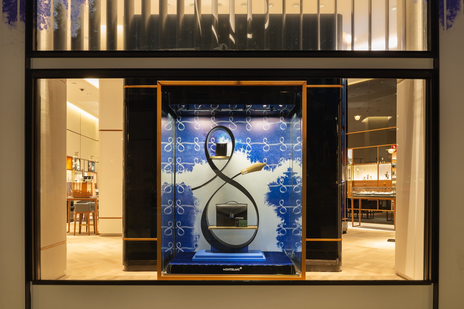 Escaparate de tienda Montblanc con un arreglo sofisticado de bolsos y accesorios contra un elegante fondo azul con patrones elegantes.