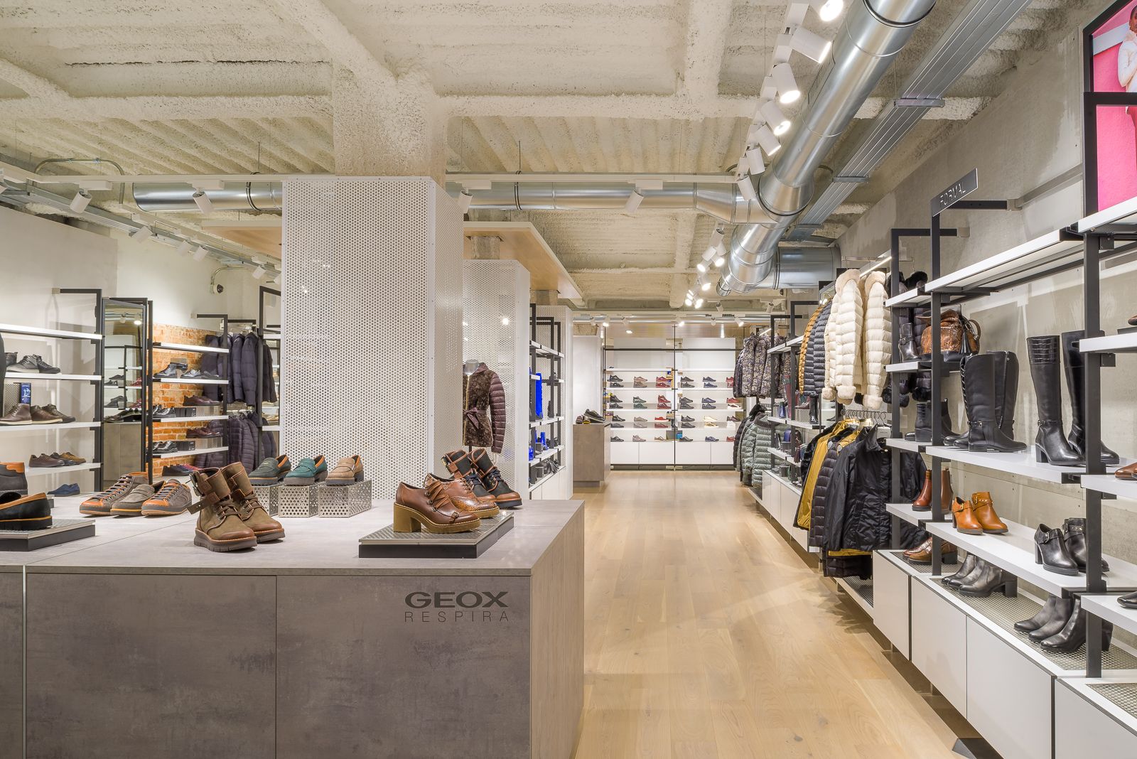 Interior de la tienda Geox que muestra una variedad de zapatos y prendas de exterior, con un diseño de techo industrial moderno.