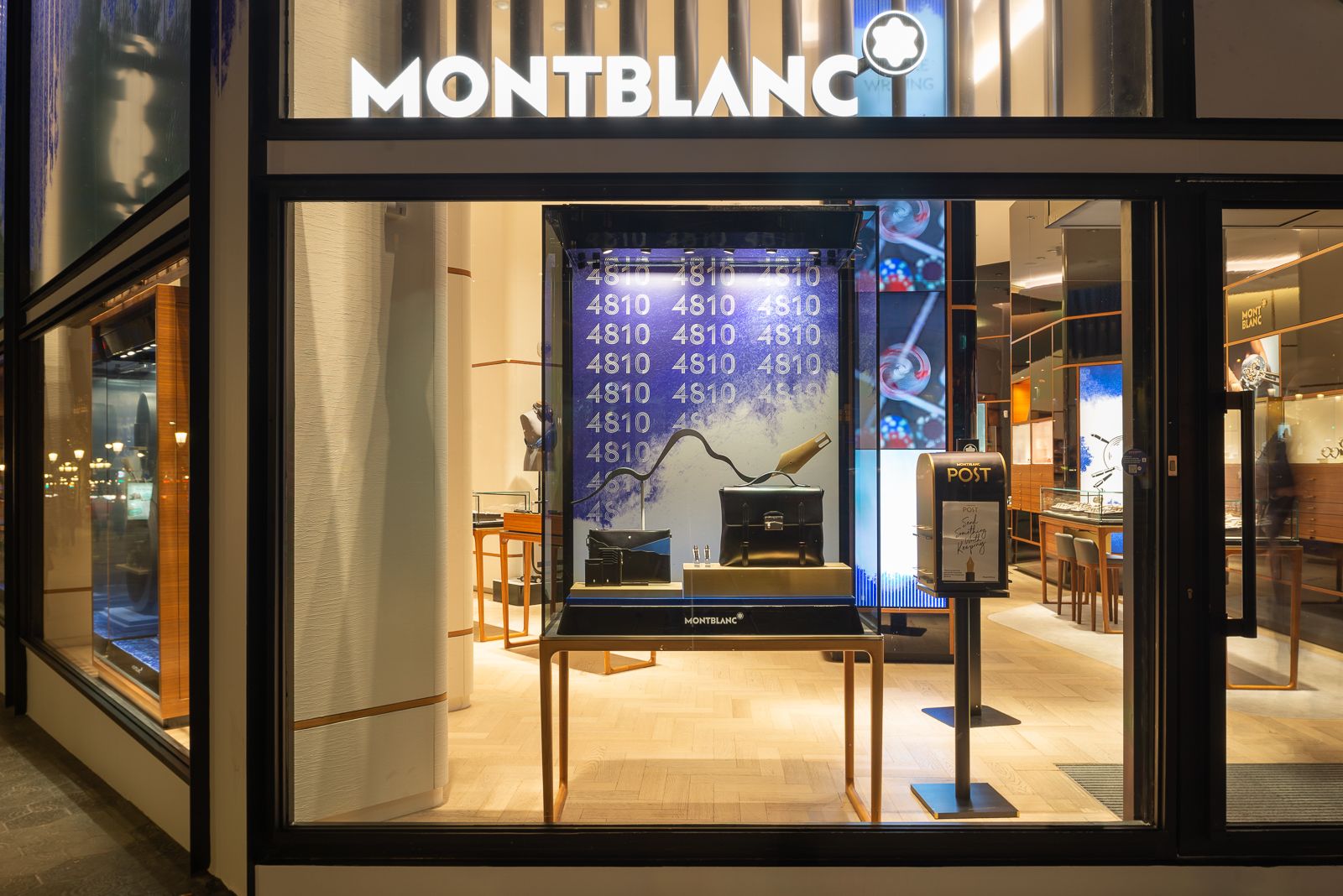 Escaparate de tienda Montblanc con un bolso negro y accesorios contra un fondo de números y un diseño artístico azul.