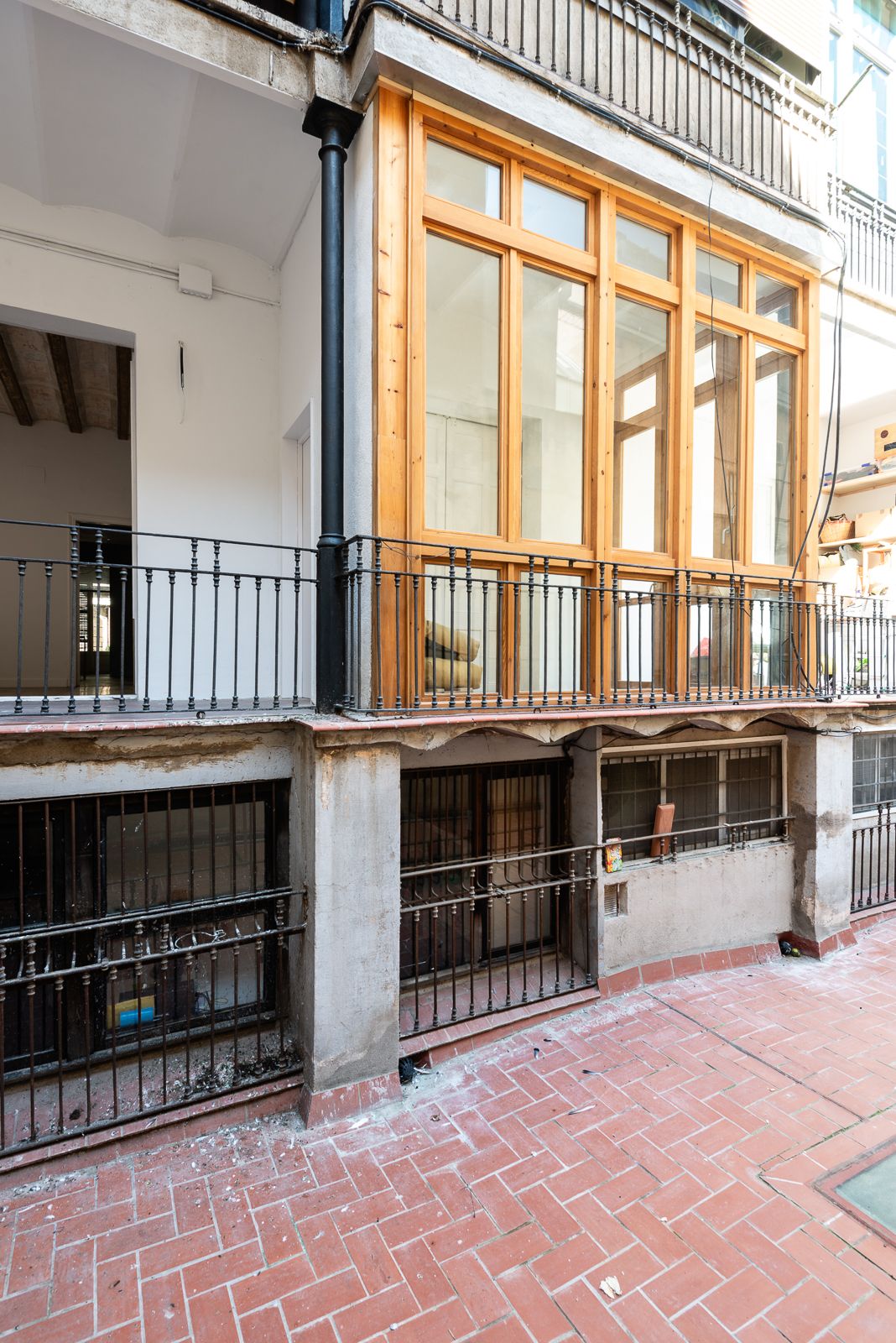 Balcón renovado con marcos de madera y barandillas de hierro con vistas a un patio de ladrillos.
