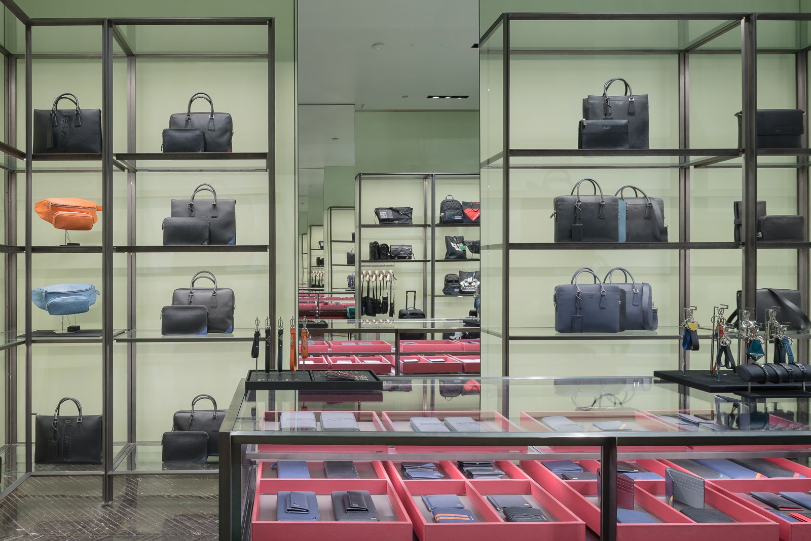 Interior de tienda Prada con dos espejos enfrentados con efecto de espejo infinito, hay estantes de bolsos de diseño en varios colores, organizados ordenadamente contra un fondo verde claro.