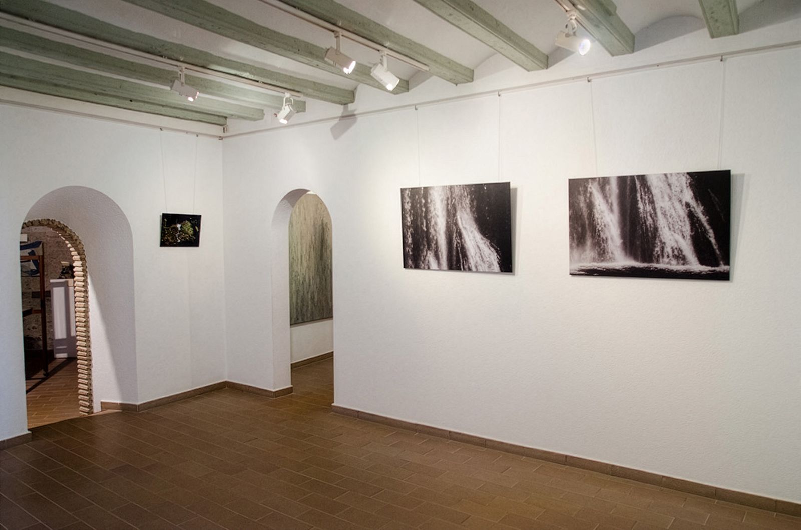 Gallery with wooden ceiling beams, tiled floor, and waterfall photographs on white walls.