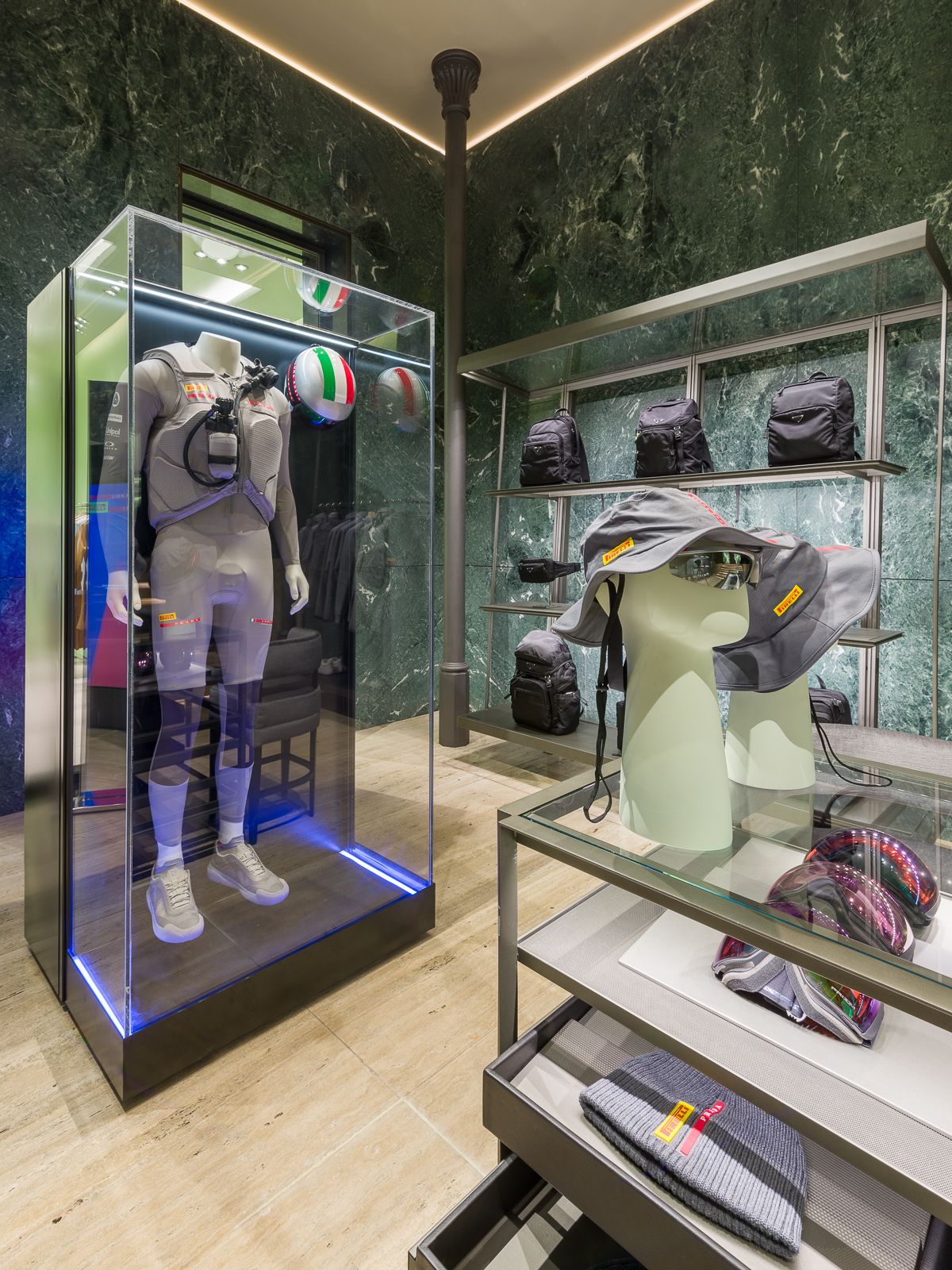 Lujosa boutique Prada con paredes de mármol verde, mostrando un maniquí en un atuendo de rendimiento encerrado en una vitrina de vidrio.