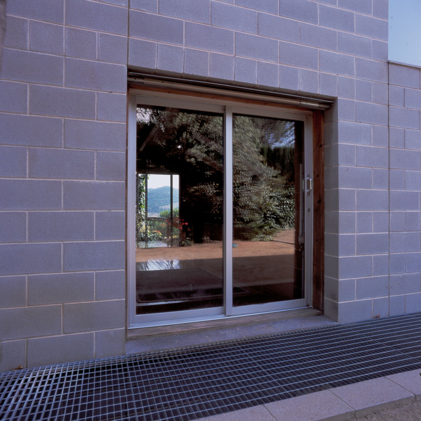 Sliding glass door on a concrete block wall, reflecting the outdoor greenery and a distant view of the hills.